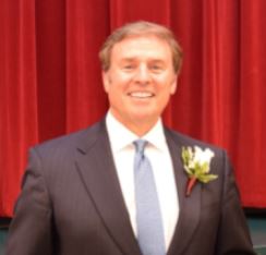 man in a suit with a flower and a red curtain backdrop